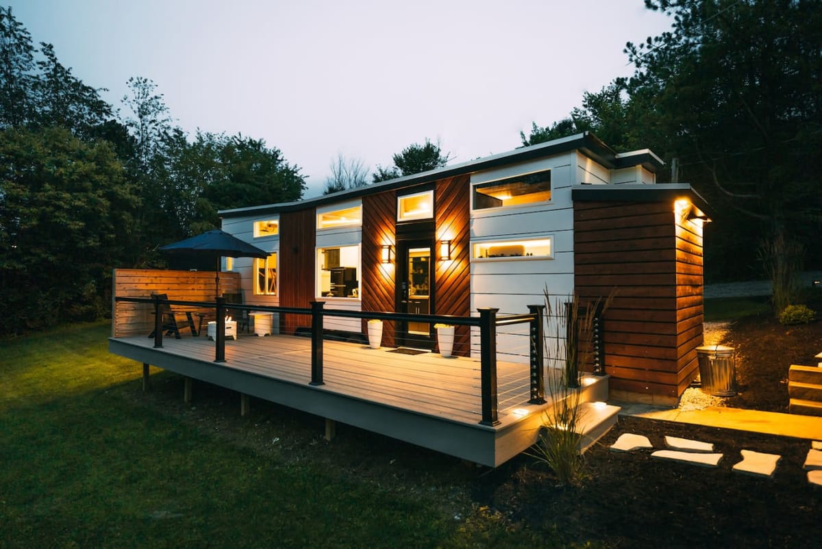 The Lux, a 32-foot modern tiny home with a full-length deck, lit up at dusk in Ohio Amish Country