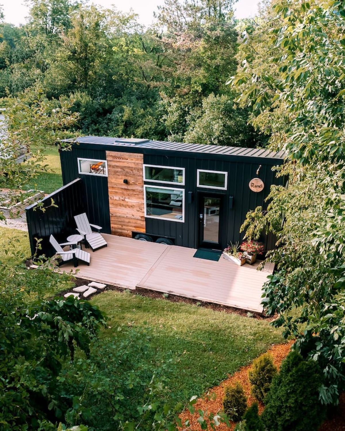 The Scandi, a black cedar tiny home with a wide deck, surrounded by trees in Ohio Amish Country