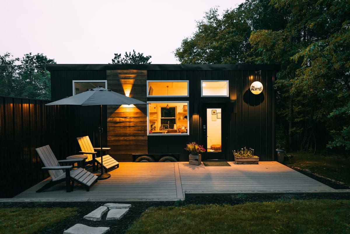 The Scandi tiny home glowing at dusk, black cedar siding and a lit deck, near Berlin, Ohio