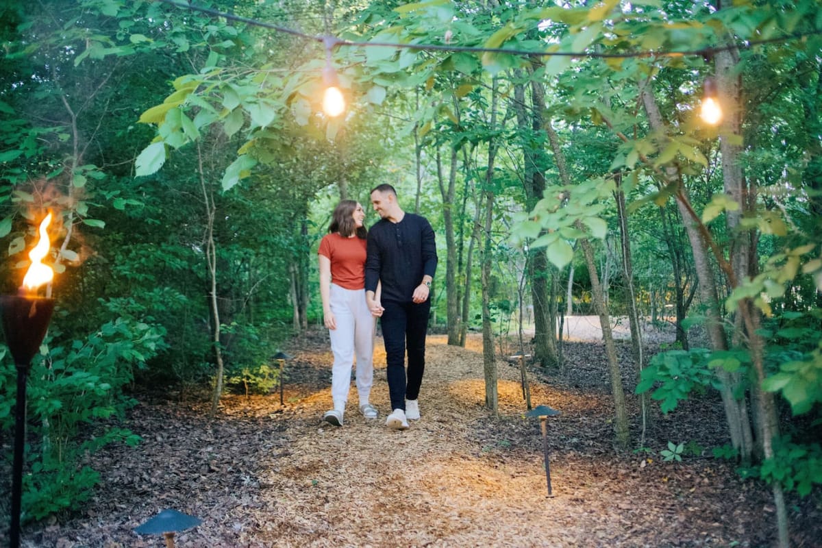 A couple walking the lit path through the woods to The Scandi tiny home