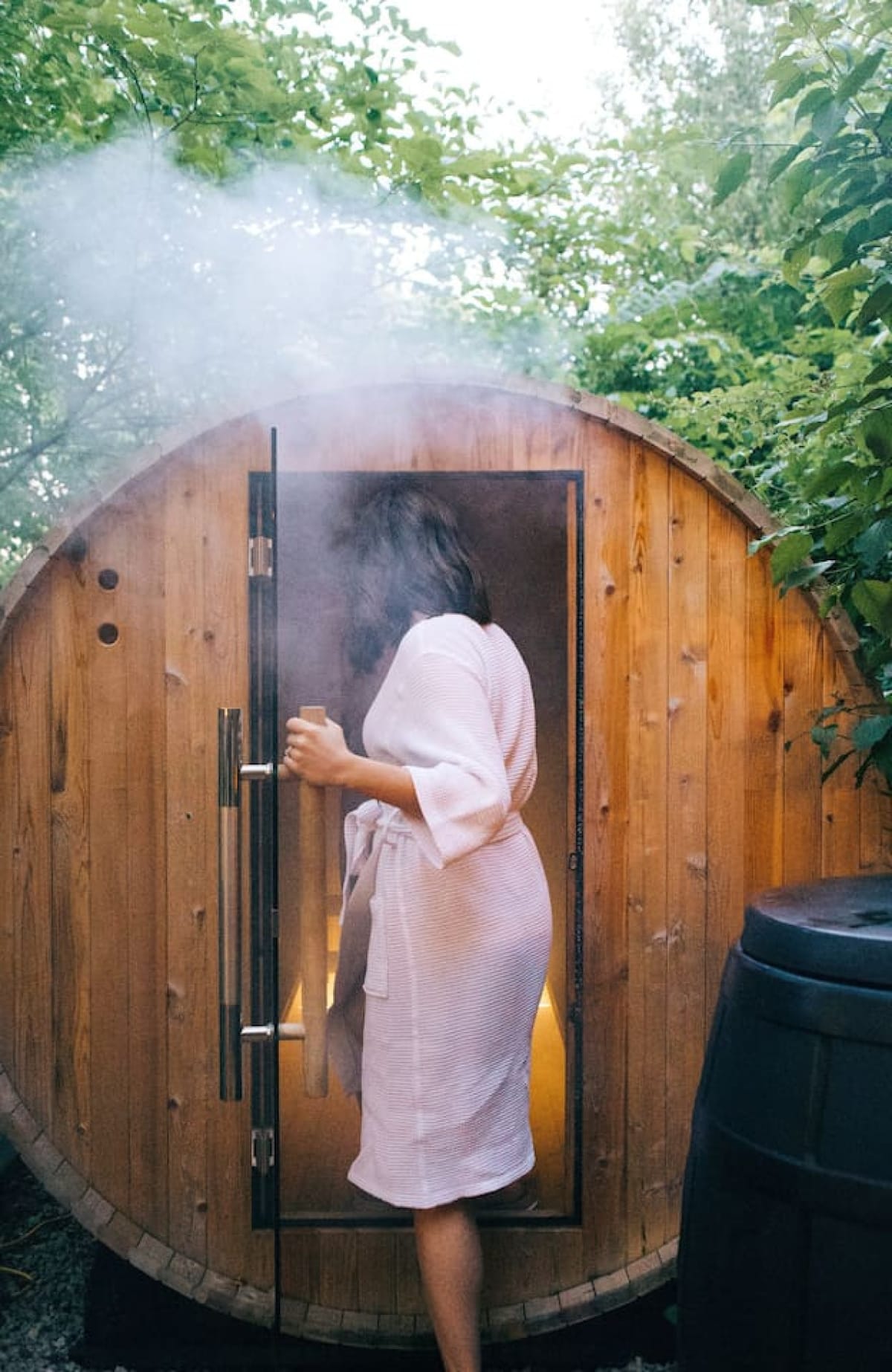 A guest in a robe opening the door of the private cedar barrel sauna at The Scandi tiny home in Berlin, Ohio